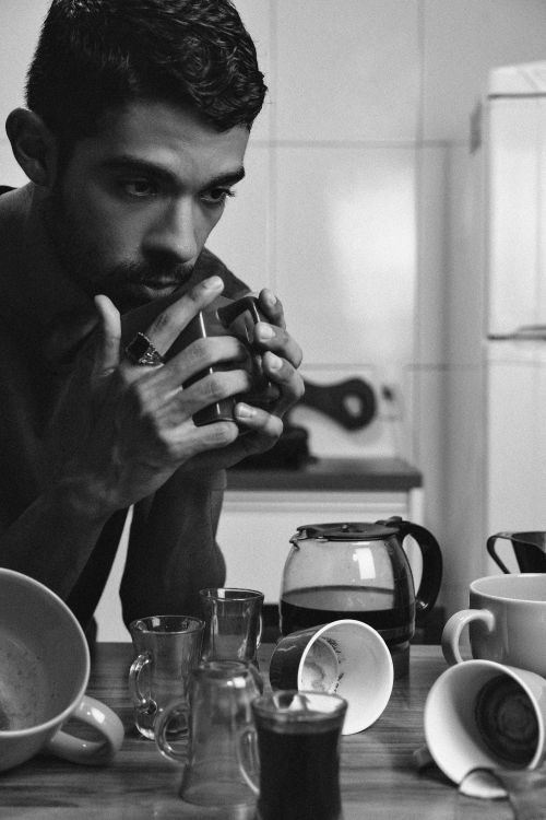 Free A contemplative man holds a mug in a modern kitchen surrounded by cups and a pot. Stock Photo