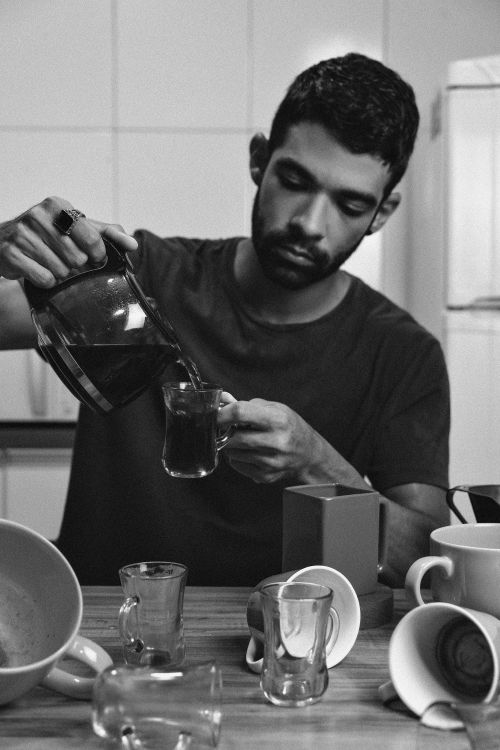 Free A man pouring coffee into a mug, surrounded by cups on a kitchen table. Stock Photo