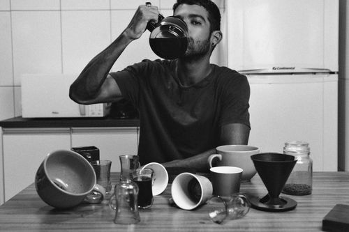 Free Man drinks coffee from a jug amid mugs and cups on a table. Stock Photo