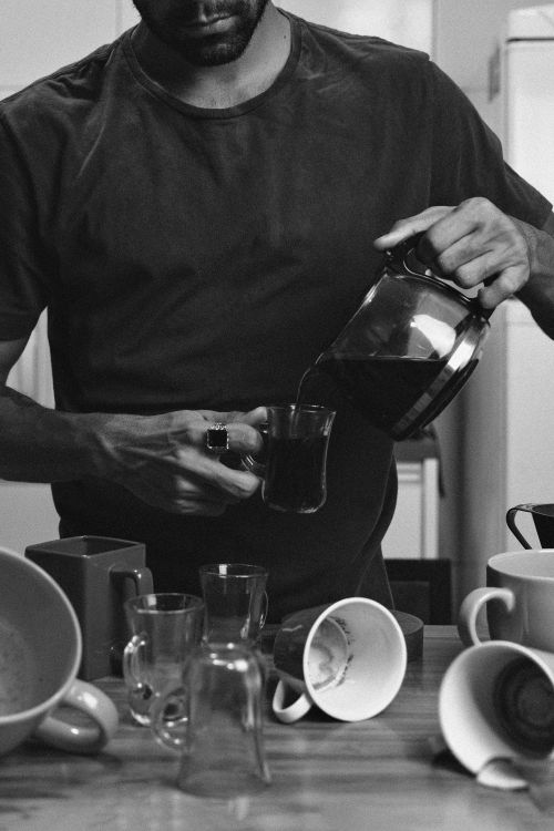 Free Man pouring coffee into a glass mug amidst scattered cups, embracing a peaceful morning routine. Stock Photo