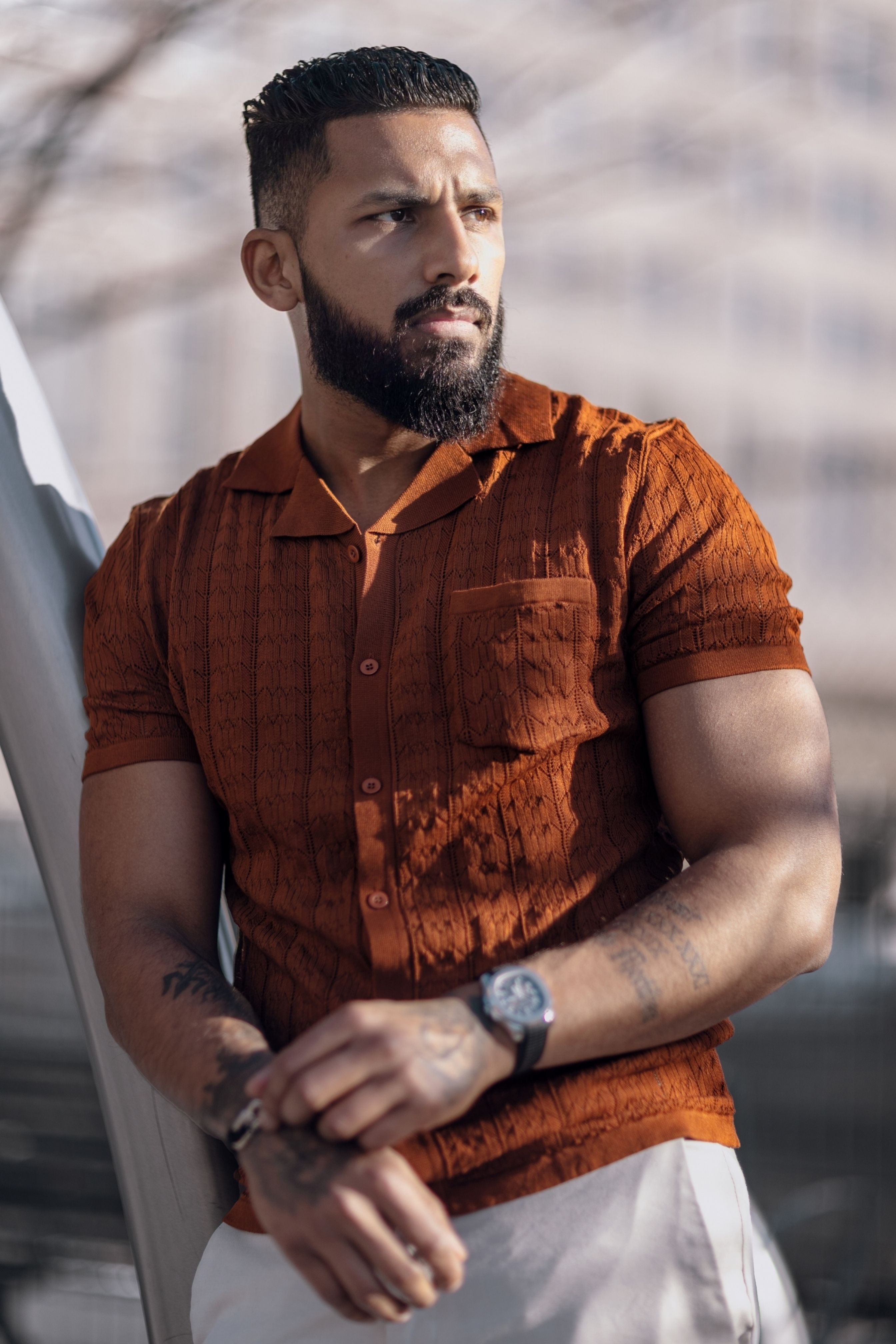 Confident man in orange shirt with beard in sunlight, fashion portrait.