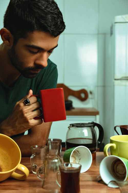 Free Thoughtful man with coffee mugs in kitchen, surrounded by cups and a coffee pot. Stock Photo