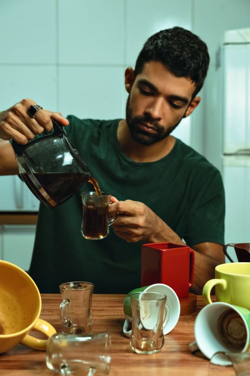 Free A focused adult male pours coffee into mugs on a kitchen counter. Stock Photo
