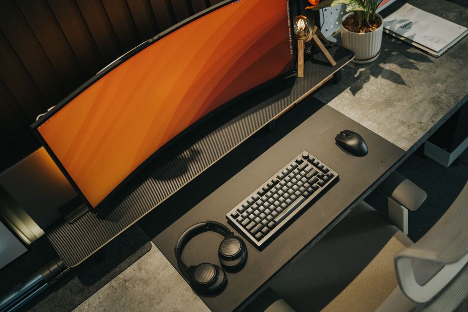 A sleek gaming desk arrangement featuring a curved monitor, keyboard, mouse, and headphones in neutral tones.