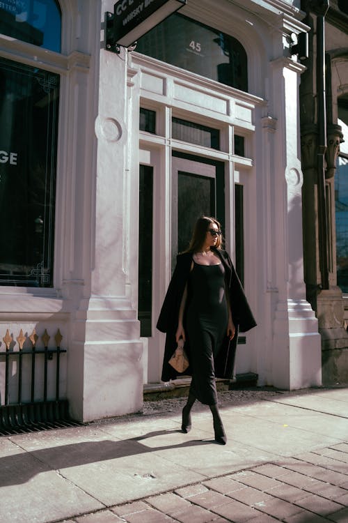 A woman in a black dress and coat walking down the street