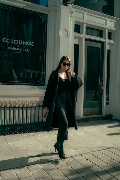 A woman in a black coat and sunglasses walking down the street