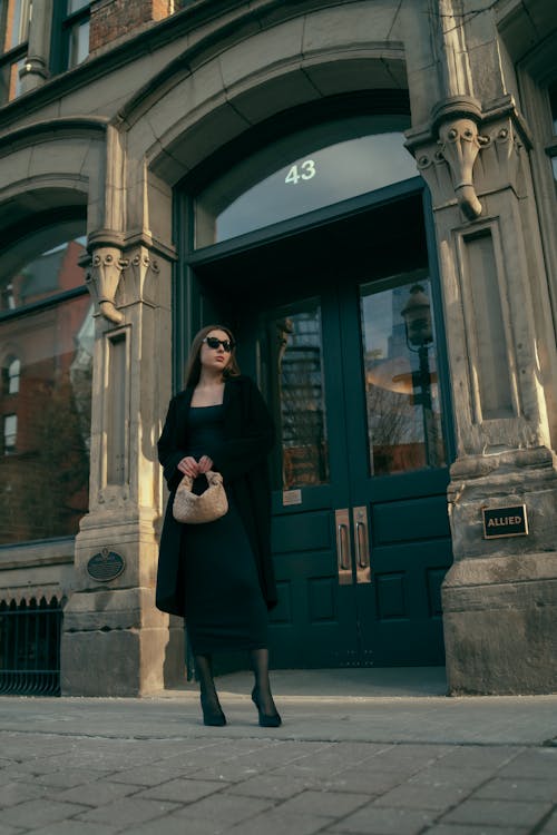 A woman in a black coat and hat standing outside a building