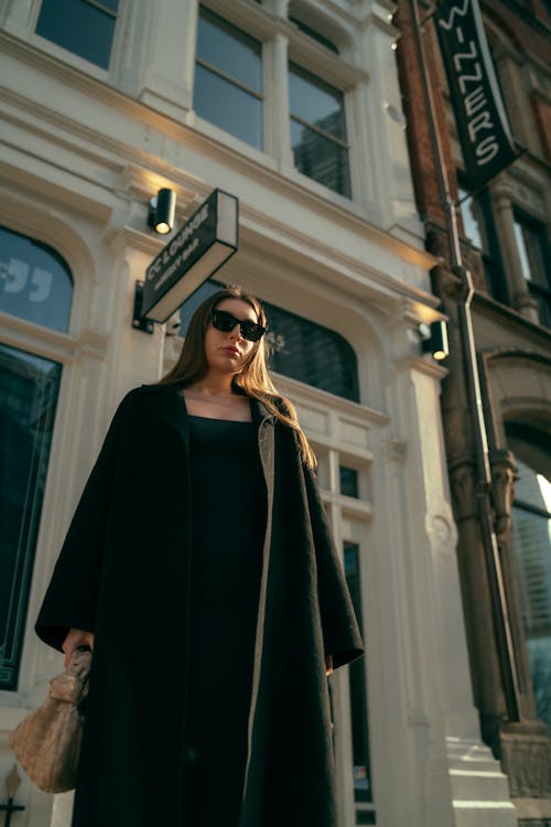 A woman in a black coat and sunglasses standing outside a building