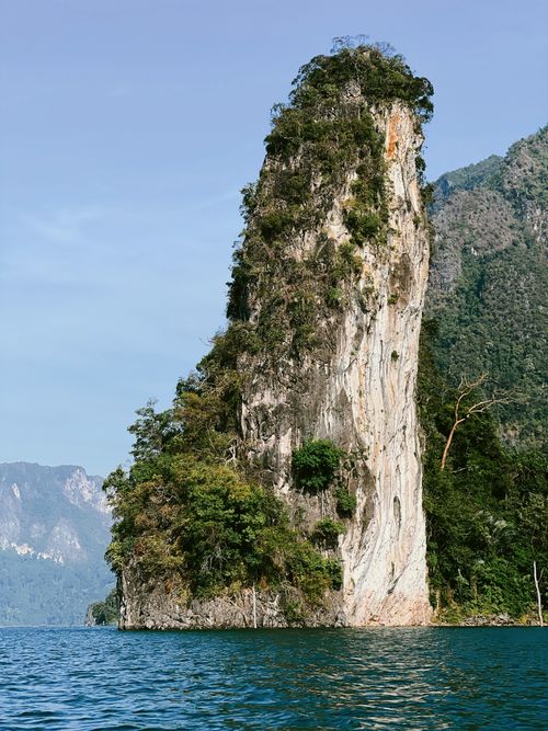 Free Tall limestone rock formation surrounded by calm blue sea and lush greenery. Stock Photo