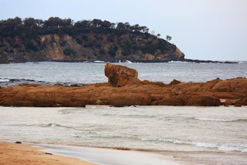 A man is walking on the beach near a rock