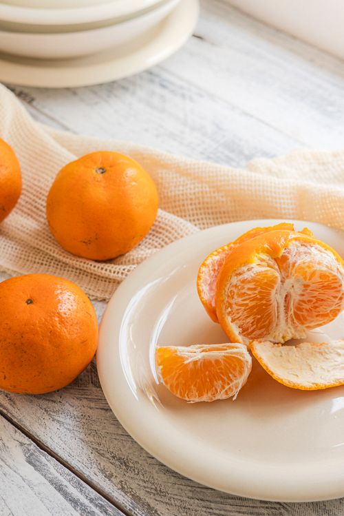Free A rustic still life of fresh tangerines, peeled and unpeeled, on a white plate. Stock Photo