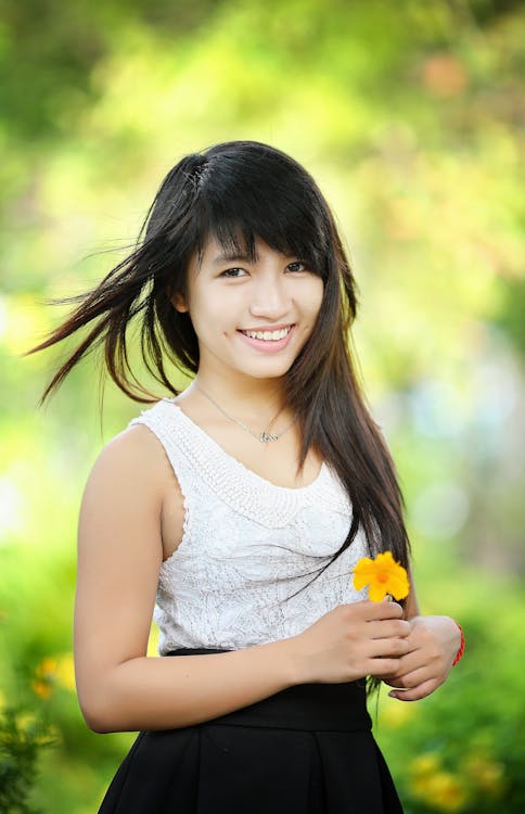 Woman Wearing White and Black Sleeveless Dress Holding Yellow Flower Selective-focus Photography