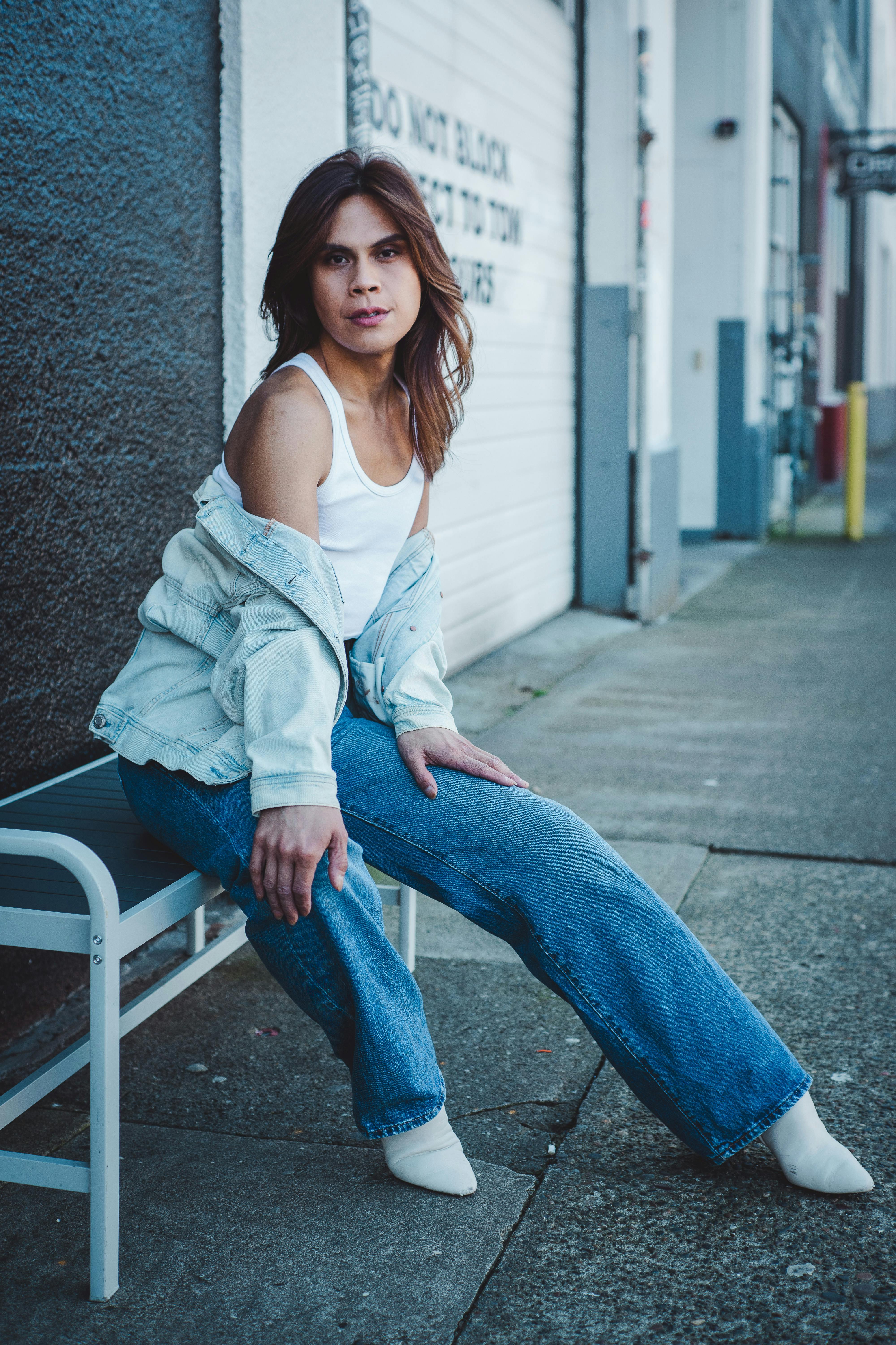 Woman in denim and white top sits on an urban street bench, exuding fashion and style.