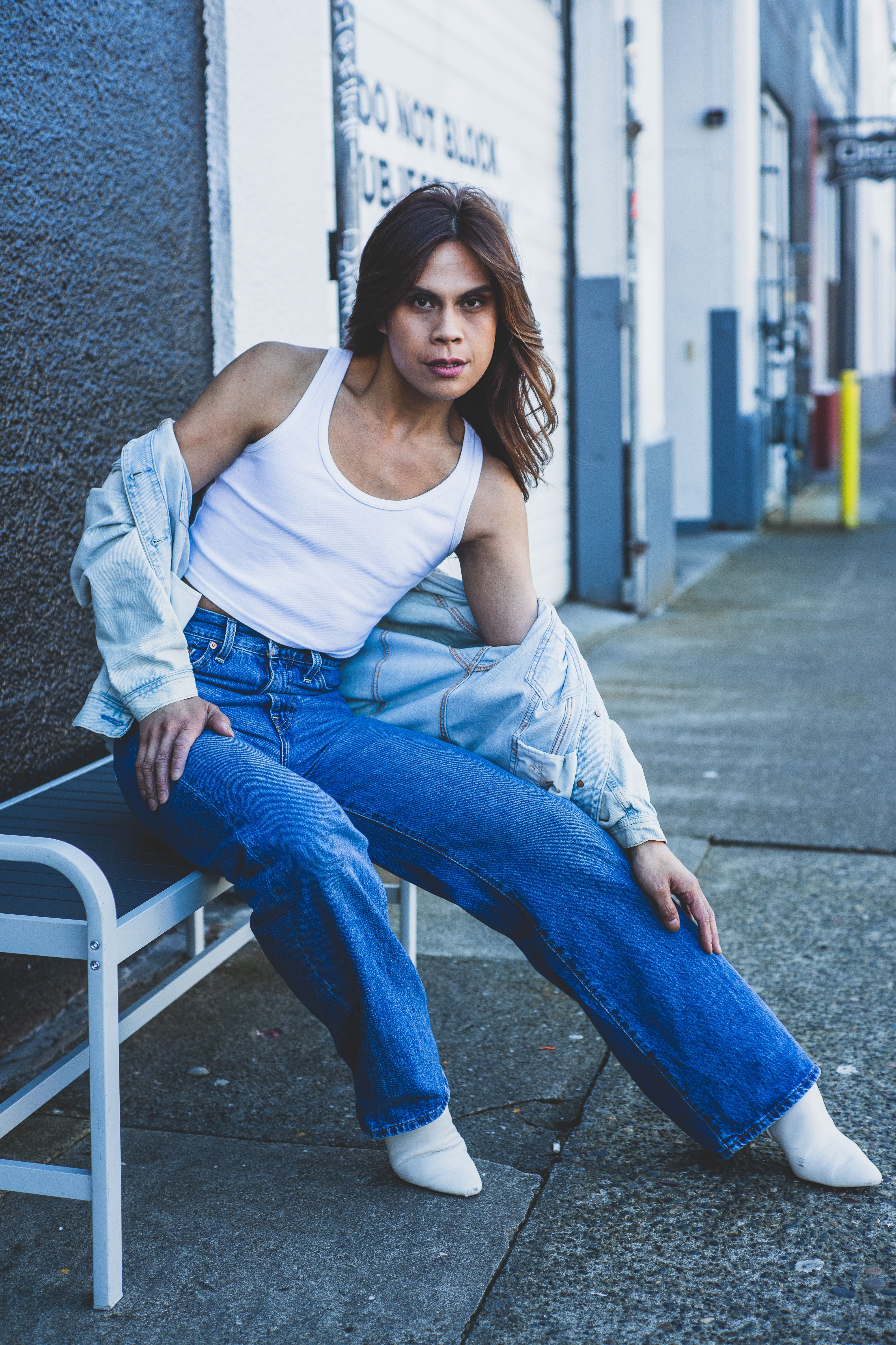 Stylish model poses in denim outfit on urban bench street setting.