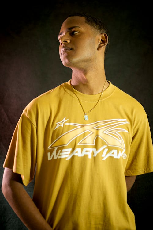 Kostenloses Stock Foto zu Gelbes T-Shirt, grauen hintergrund, halskette
