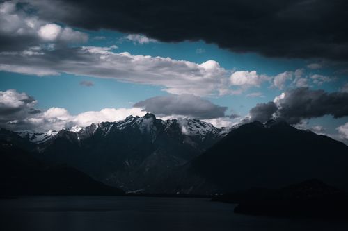 Free Breathtaking view of snow-capped mountains enveloped by moody clouds and shadows, creating a dramatic nature scene. Stock Photo