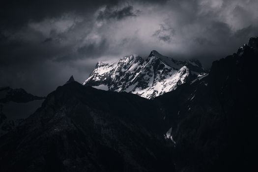 A moody, atmospheric shot of a snow-covered mountain peak shrouded in dark, stormy clouds.