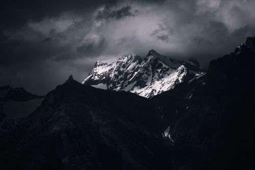 Free A moody, atmospheric shot of a snow-covered mountain peak shrouded in dark, stormy clouds. Stock Photo