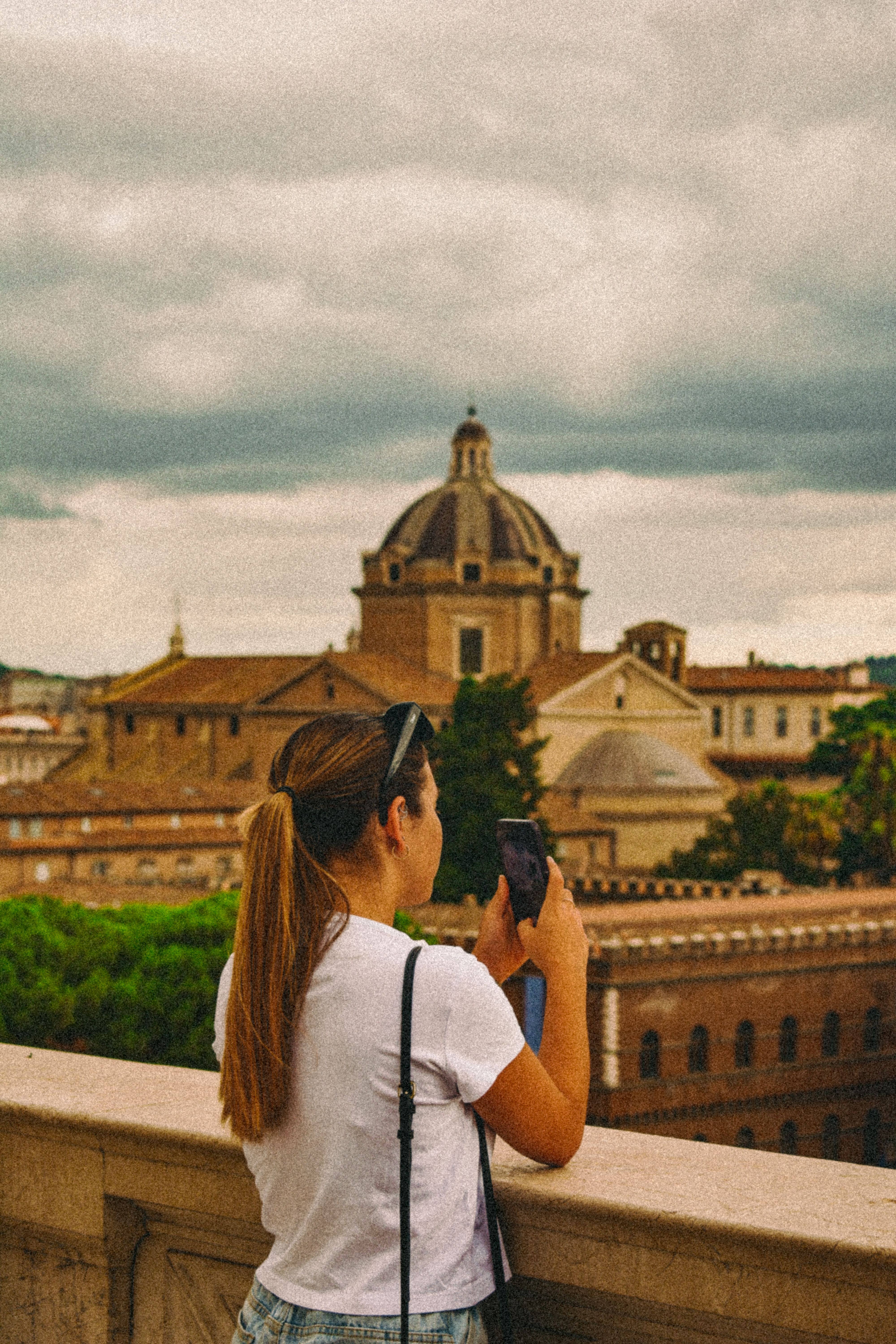 A young woman captures the stunning Rome skyline with her smartphone on an observation deck.