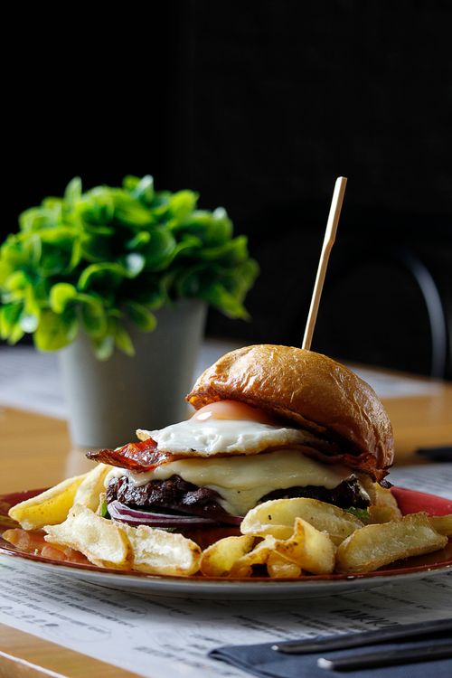 Free Mouth-watering gourmet burger topped with bacon and egg, served with crispy fries at a restaurant. Stock Photo