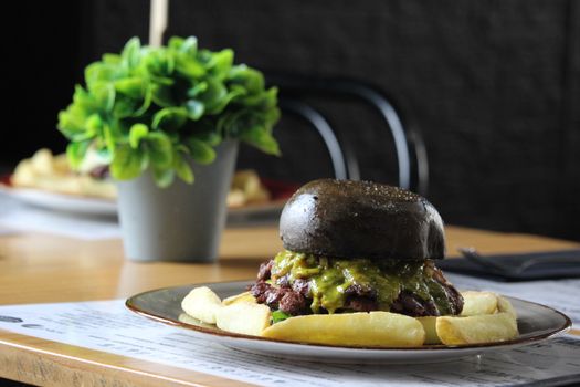 Delicious gourmet burger in a charcoal bun served with fries and a side salad in a restaurant setting.