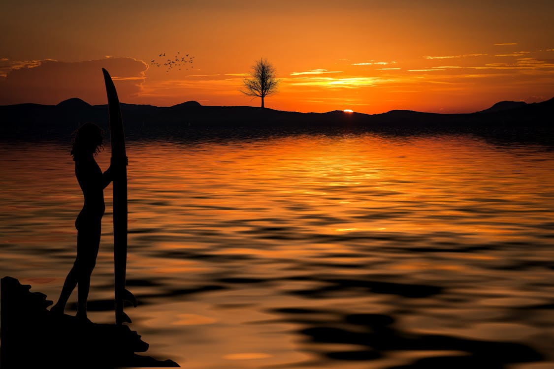 Free Person Holding a Surfboard Near the Sea on a Setting Sun Stock Photo