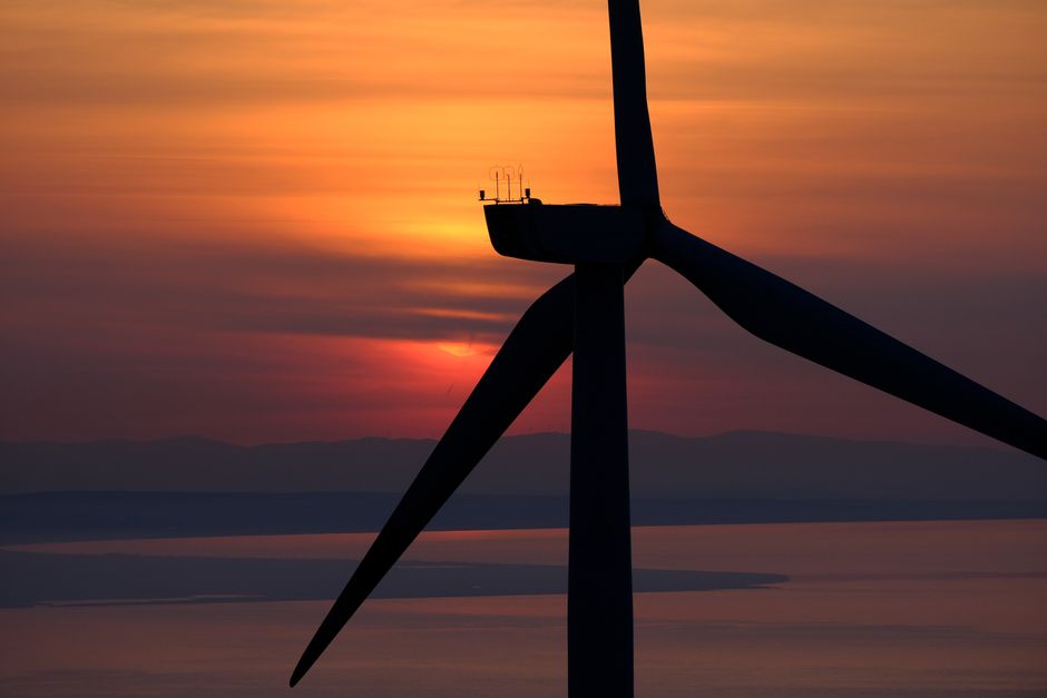 A dramatic silhouette of a wind turbine against a vibrant sunset over the sea, highlighting renewable energy.