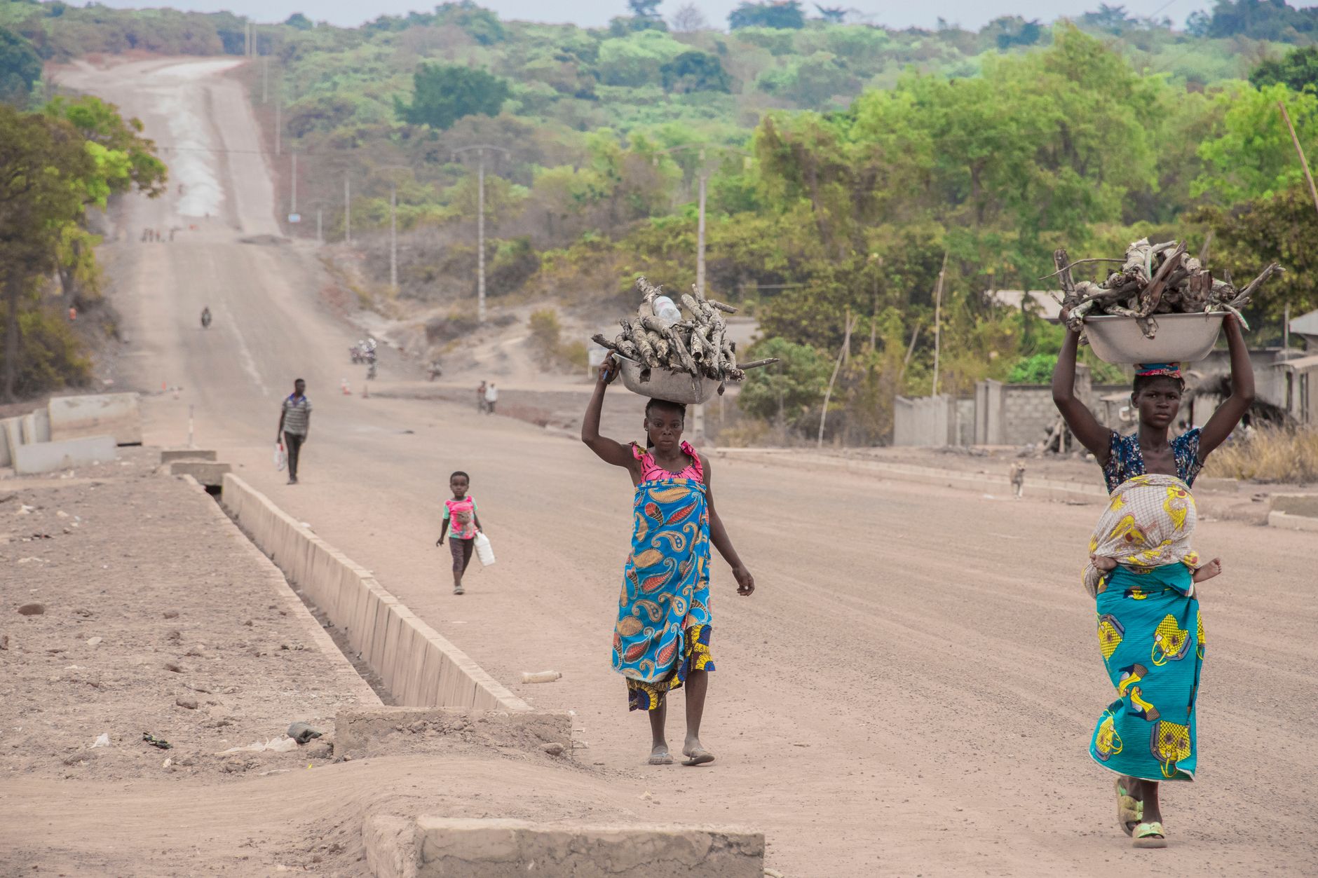 African women carrying wood on their heads along a rural road, symbolizing daily life in the countryside.