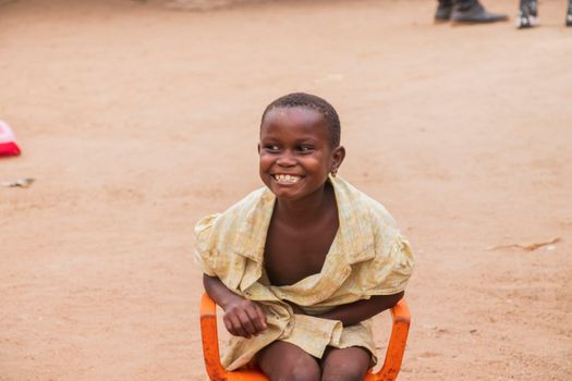 Happy African child sitting on a chair outdoors, radiating a joyful smile.