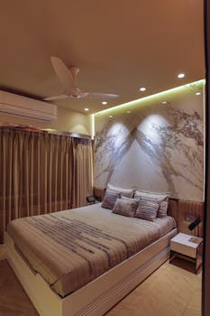 Stylish bedroom with ambient lighting and contemporary decor features a ceiling fan and artistic wall design.