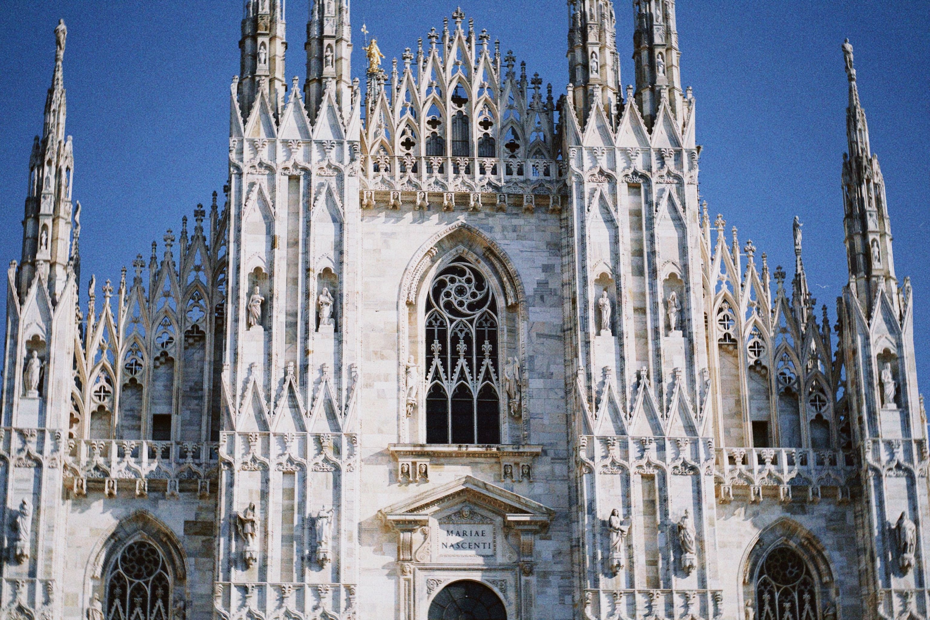 Close-up view of the intricate Gothic facade of Milan Cathedral in Italy against a clear blue sky.