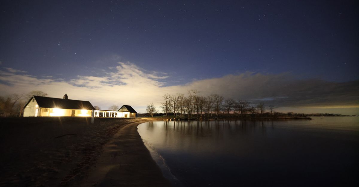 A serene night view of an illuminated house by a tranquil lake in Stamford, CT.