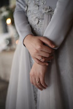Close-up of a woman in a gray dress showing hands with wedding ring, elegant bridal detail.