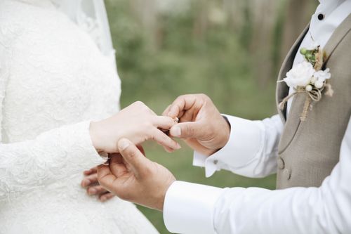 Free Close-up of a groom placing a wedding ring on the bride's finger during an outdoor ceremony. Stock Photo