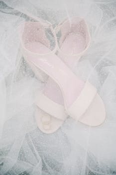 Flat lay of elegant bridal sandals and wedding rings on a bridal veil.
