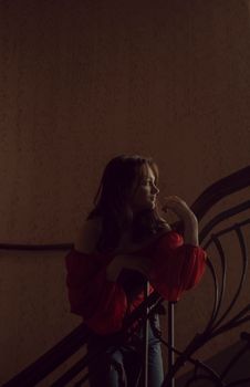 Moody portrait of a woman in a red blouse on a staircase, in dramatic lighting.