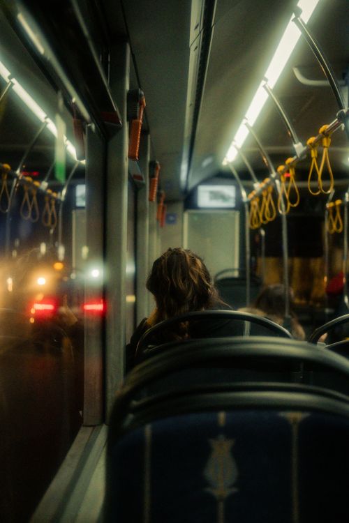 Free A woman sits inside a dimly lit bus during an evening commute, reflecting city lights. Stock Photo