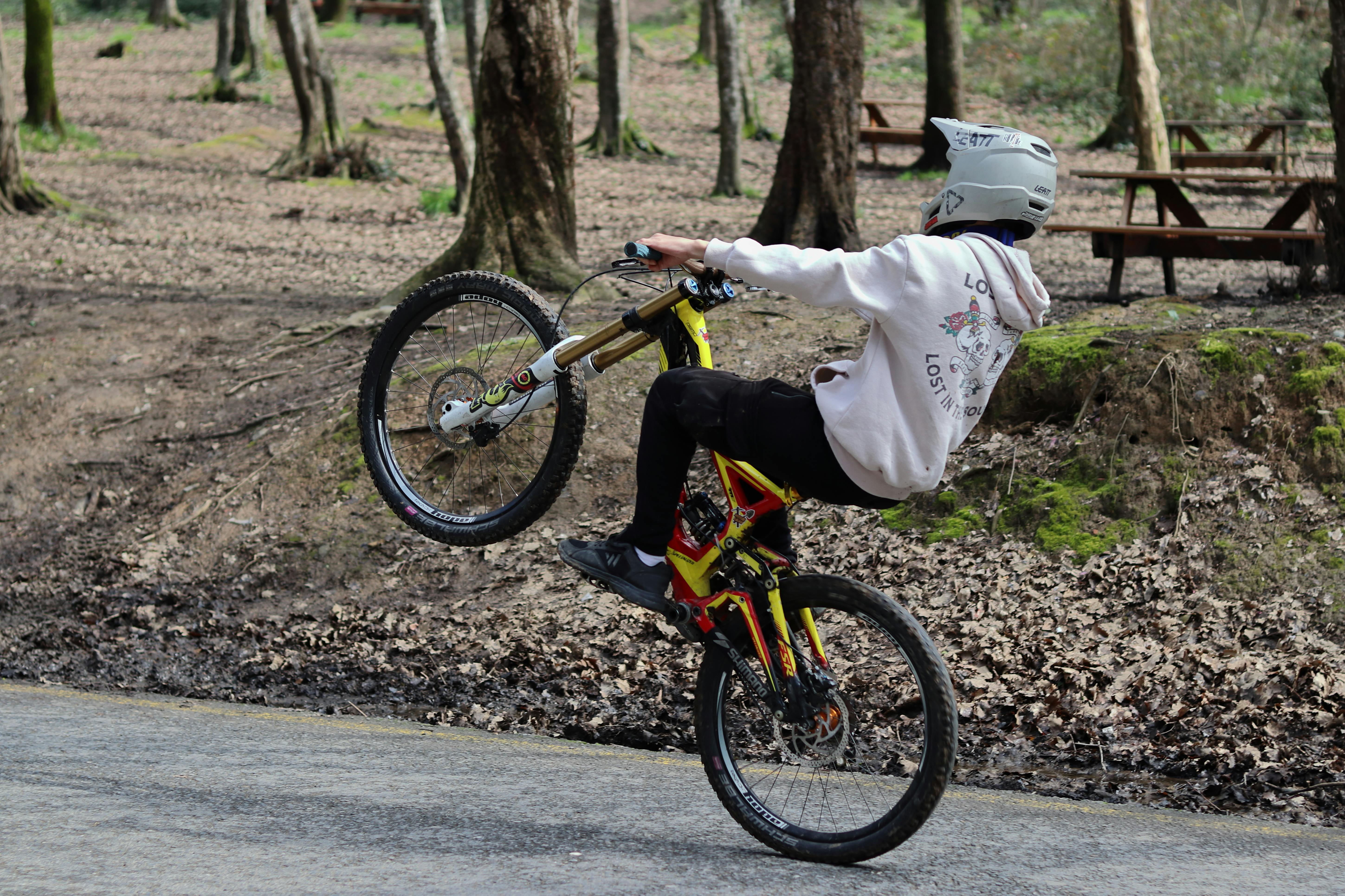 A cyclist performing a wheelie on a mountain bike in a wooded area during daytime.
