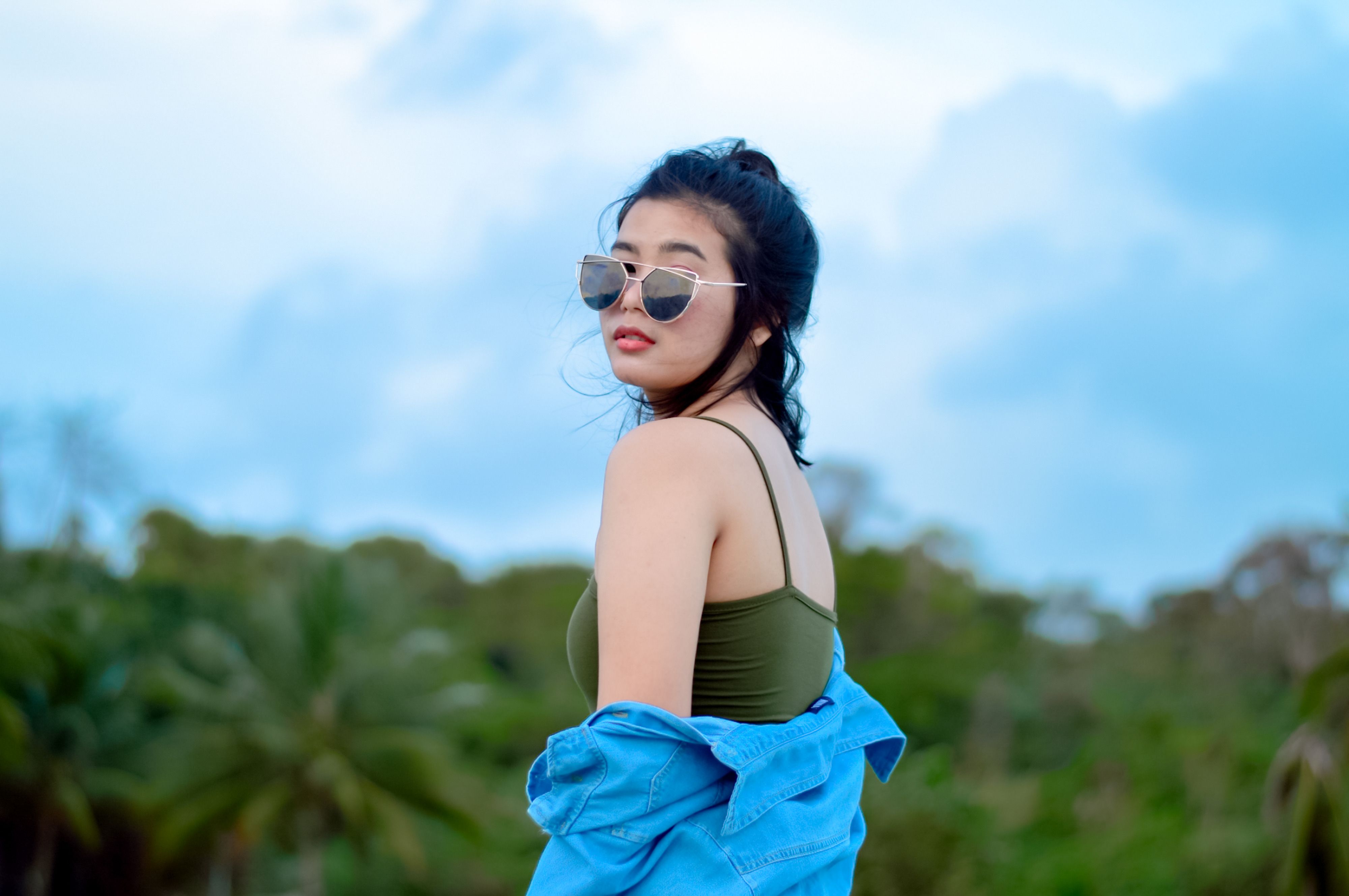 Woman in sunglasses posing stylishly outside with tropical background.
