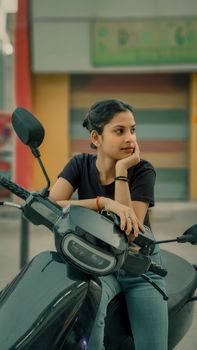 A thoughtful young woman sits on a motorbike, gazing into the distance outdoors.