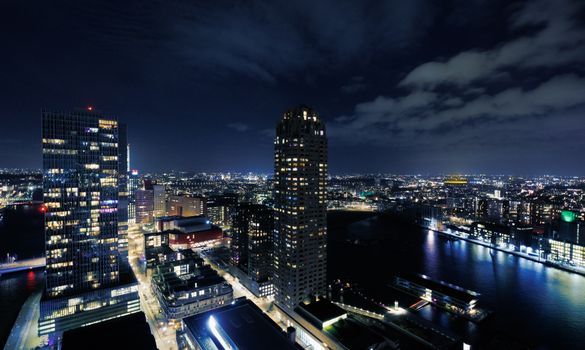 A breathtaking night cityscape of Rotterdam with illuminated skyscrapers and river reflections.