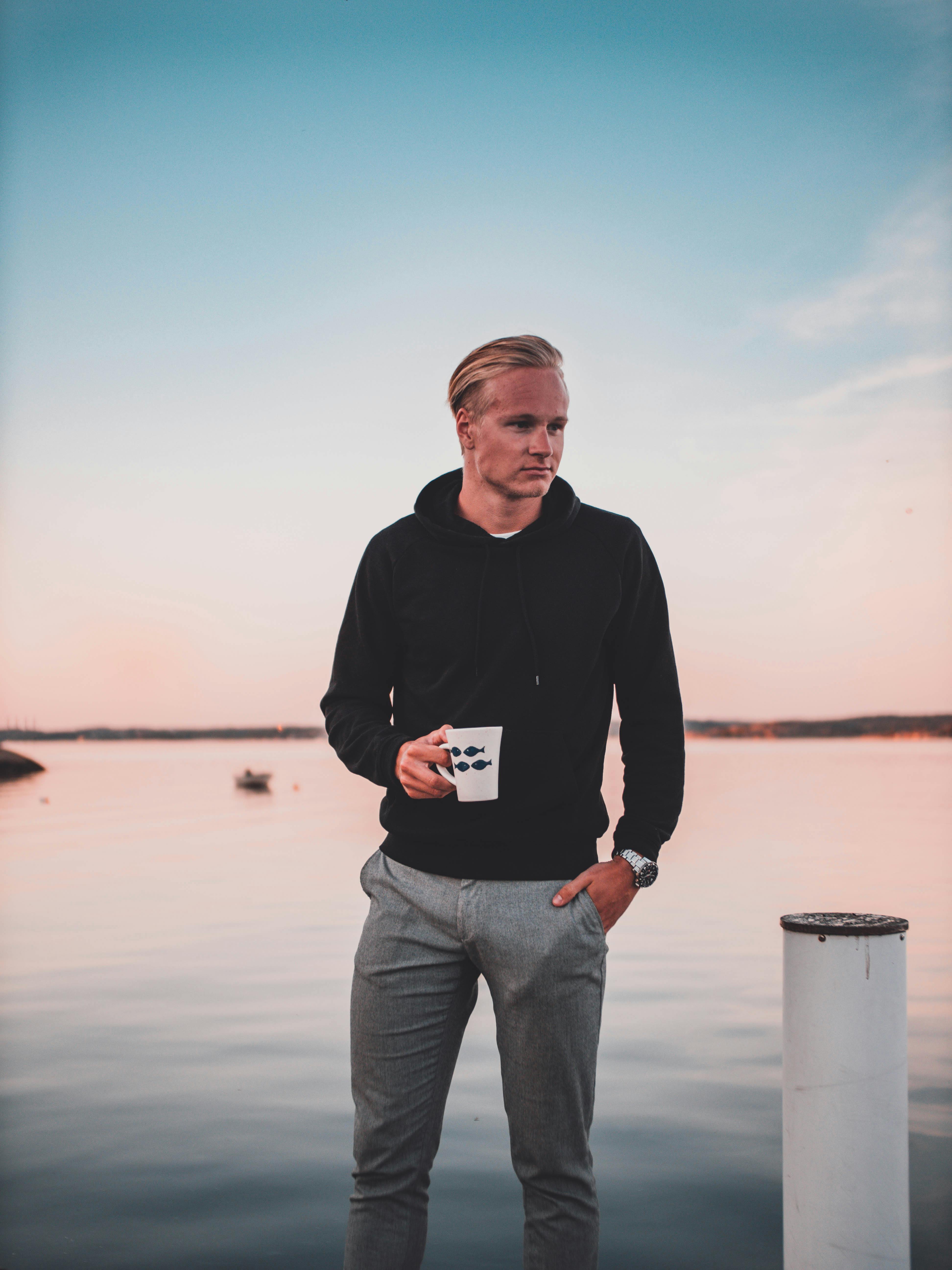 黄昏时分，一位时尚的年轻人在湖边喝着咖啡