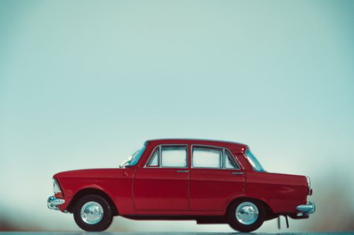 Free A detailed side view of a vintage red toy car against a pastel minimalistic backdrop. Stock Photo