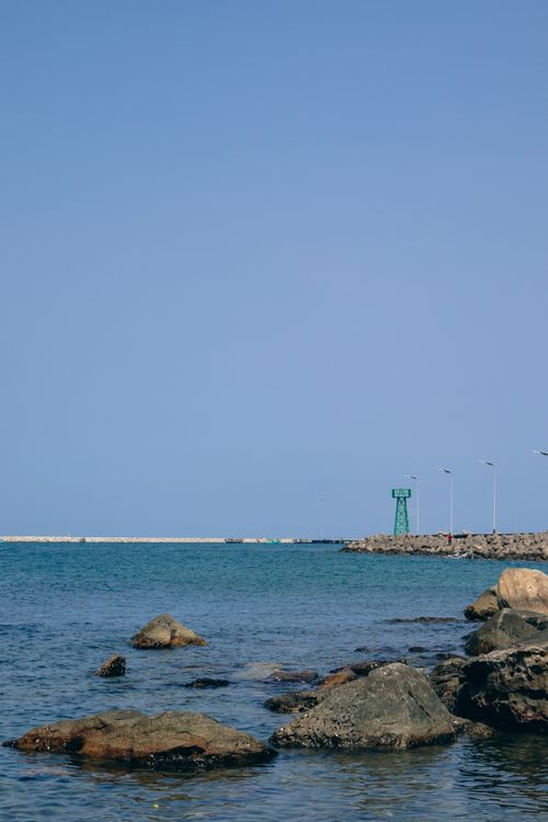 Free A tranquil coastal scene featuring rocks, a calm sea, and a clear blue sky. Stock Photo