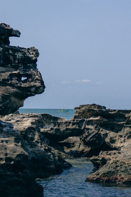 Rocky coastline with a distant boat against the serene sea in Phu Quoc, Vietnam.
