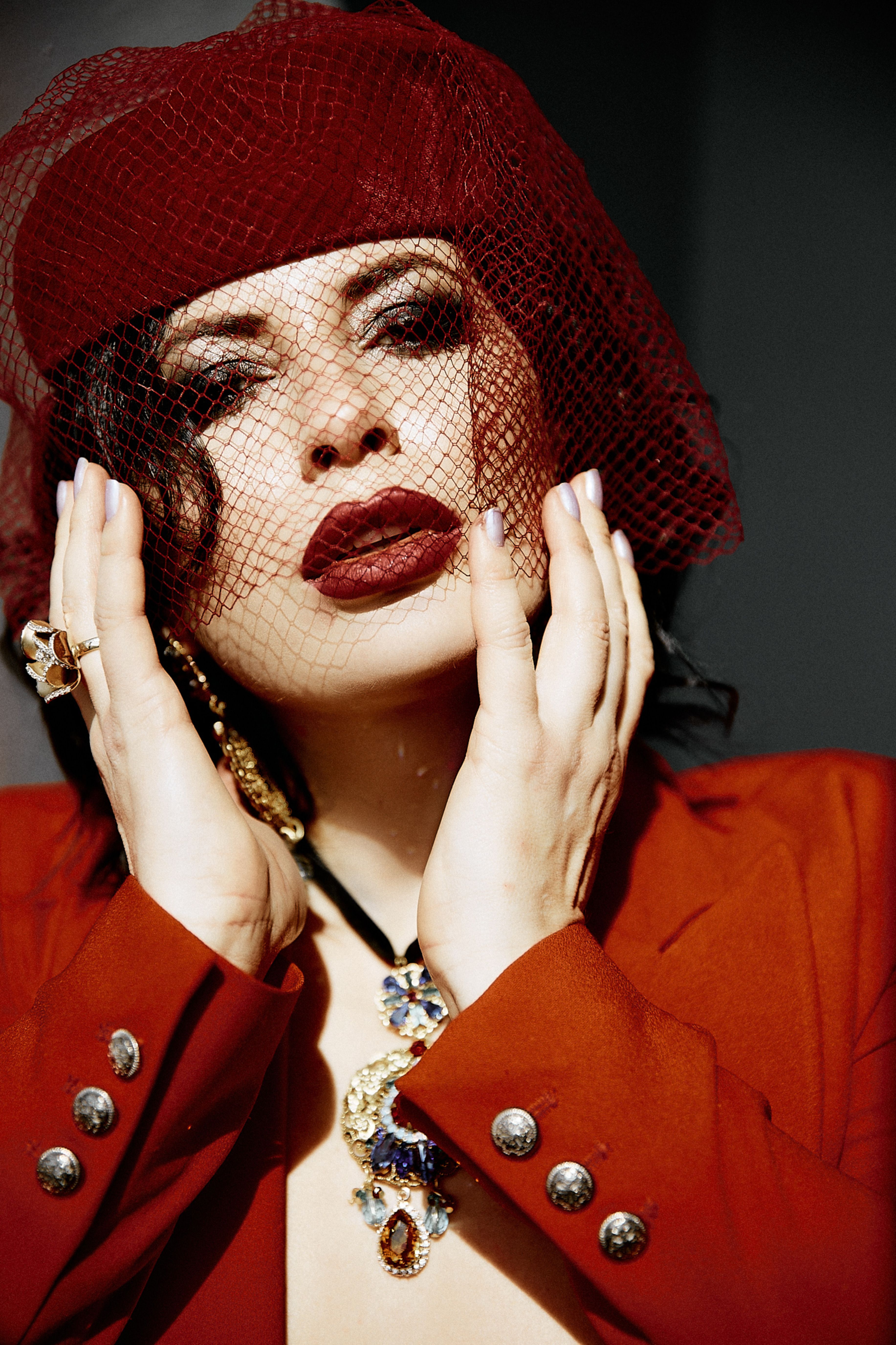 Portrait of an elegant woman in a striking red hat with veil and bold jewelry, showcasing fashion elegance.
