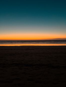 A breathtaking view of a beach at sunrise showcasing vibrant orange and blue horizons and tranquil waters.