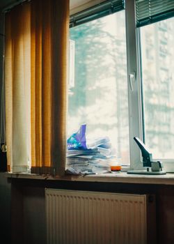 A well-lit office window with curtains, papers, and a stapler on the sill.