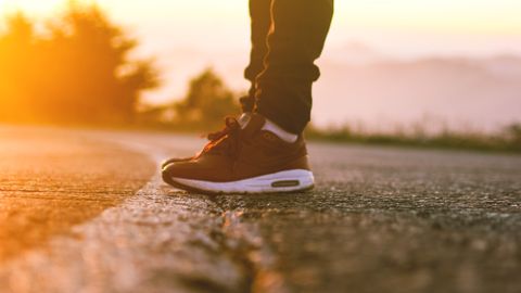 Close-up of a person's sneakers on a sunlit road in Algeria during dawn.