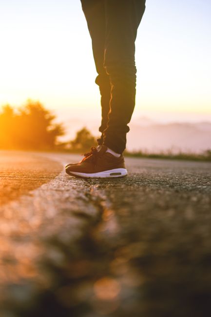 Close-up of a person's sneakers on a sunlit road in Algeria during dawn.